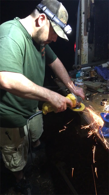 A person in a green t-shirt and cap uses a yellow angle grinder on a metal piece, creating bright sparks in a workshop.