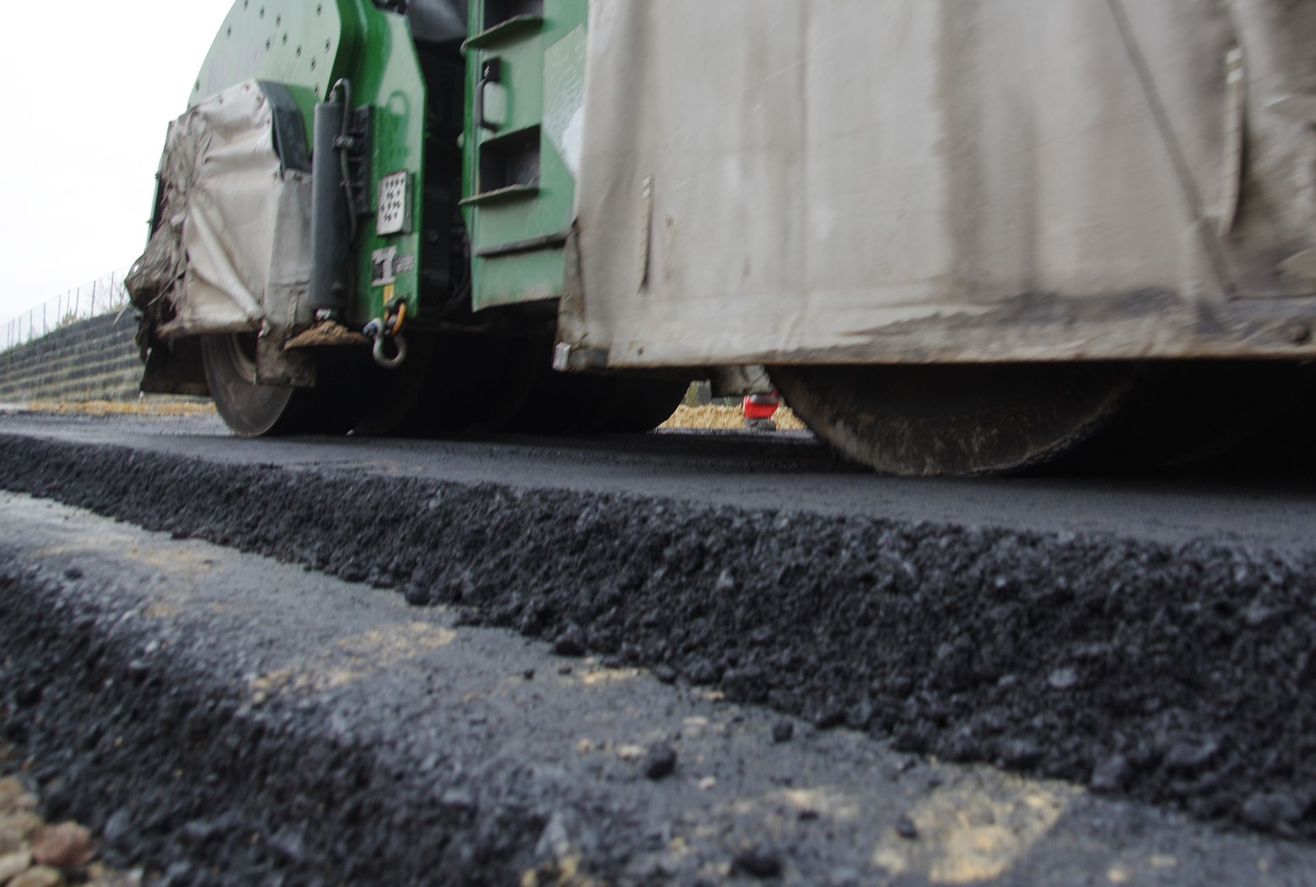 A green roller is rolling asphalt on a road.