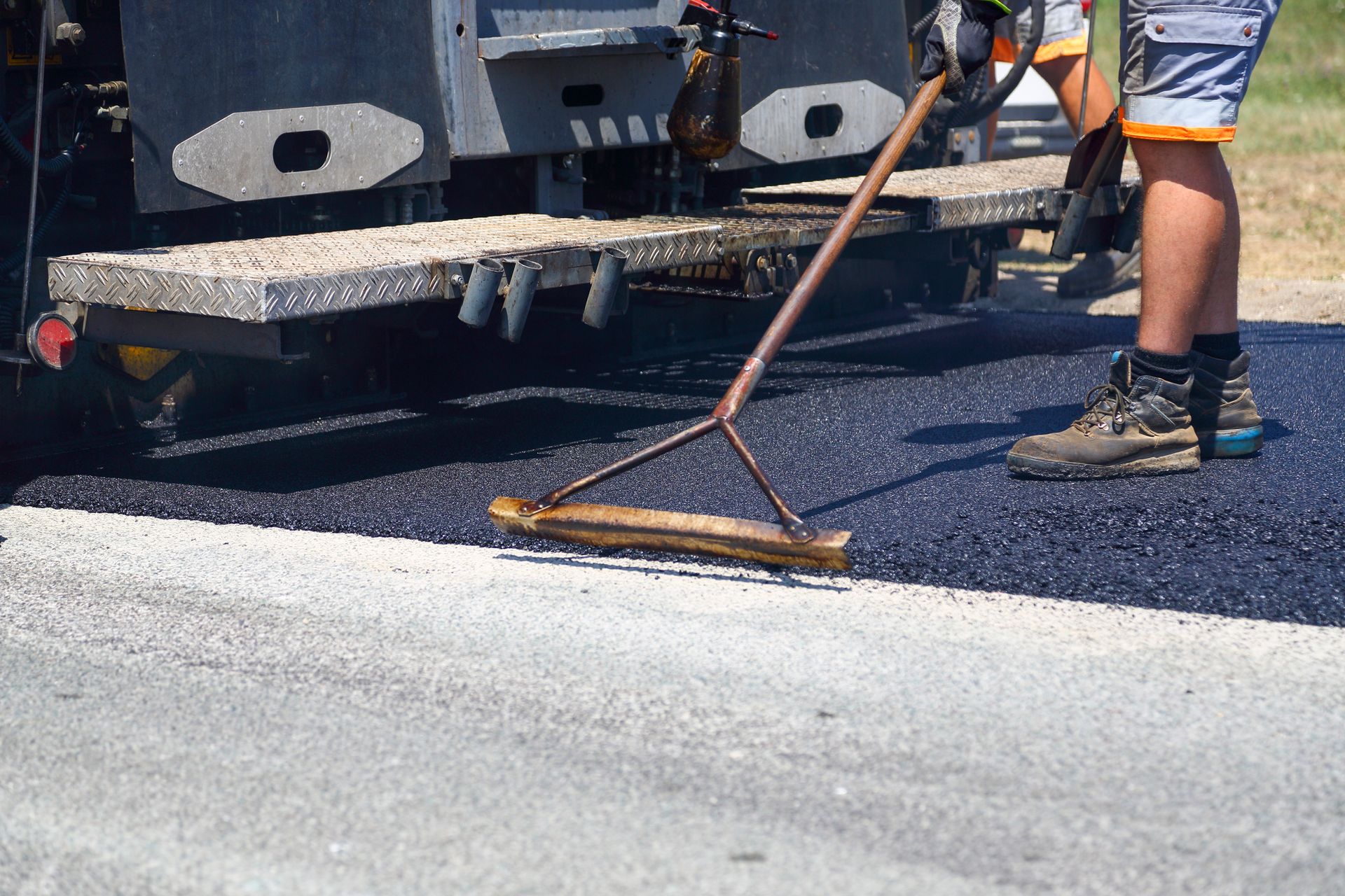 A man is using a broom to spread asphalt on a road.