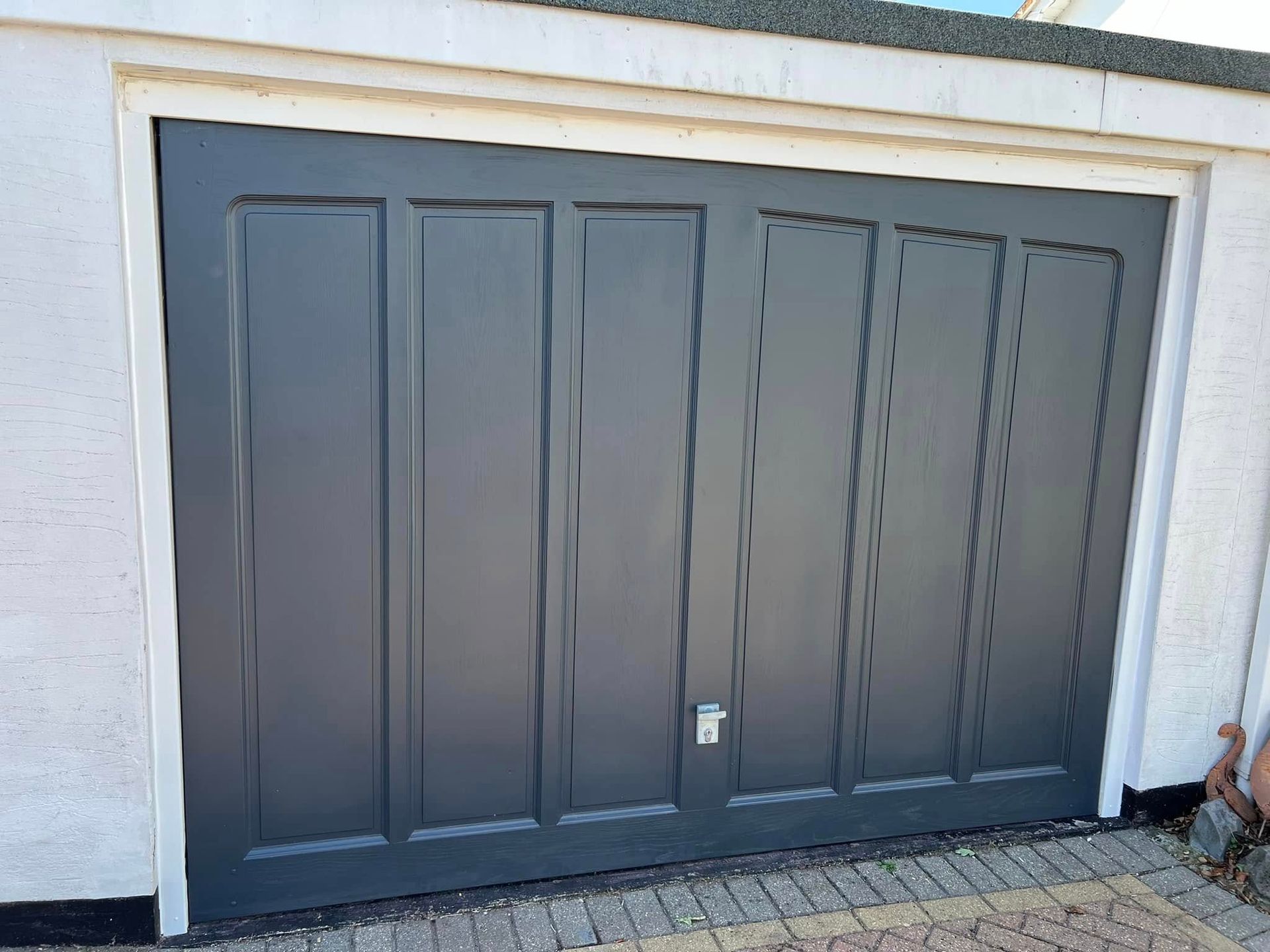 A black garage door is sitting on top of a brick driveway.