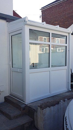 A white conservatory is sitting on the side of a house.