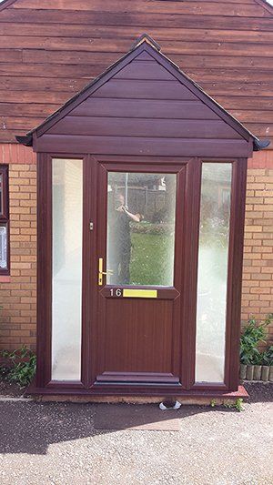 The front door of a brick house with a porch and a brown door.