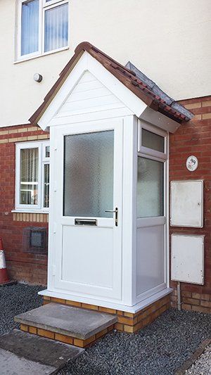 A white porch on the side of a brick house.