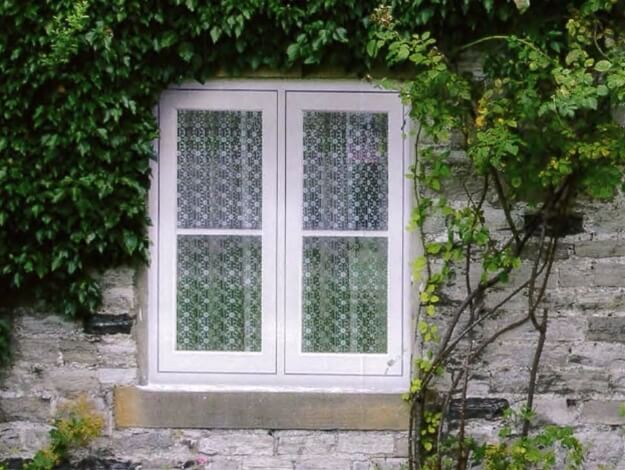 A white window on a brick wall with ivy growing around it