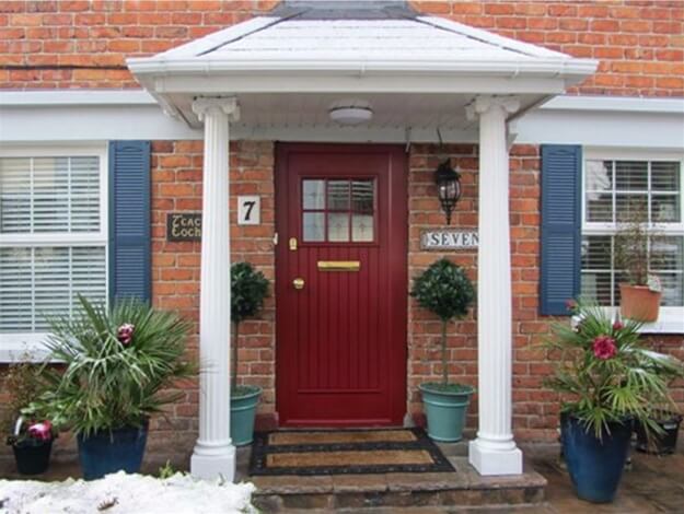 A red door is on a brick house with blue shutters.
