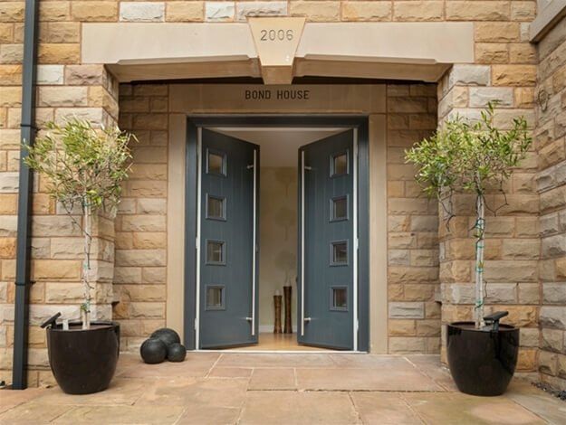 The front door of a brick building with two potted plants in front of it.