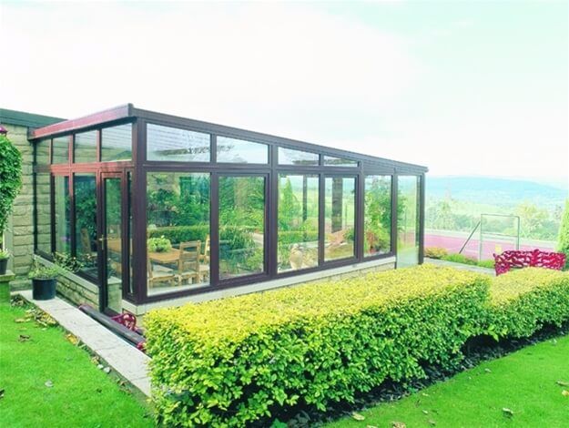 A large conservatory with a lot of windows is in the backyard of a house.