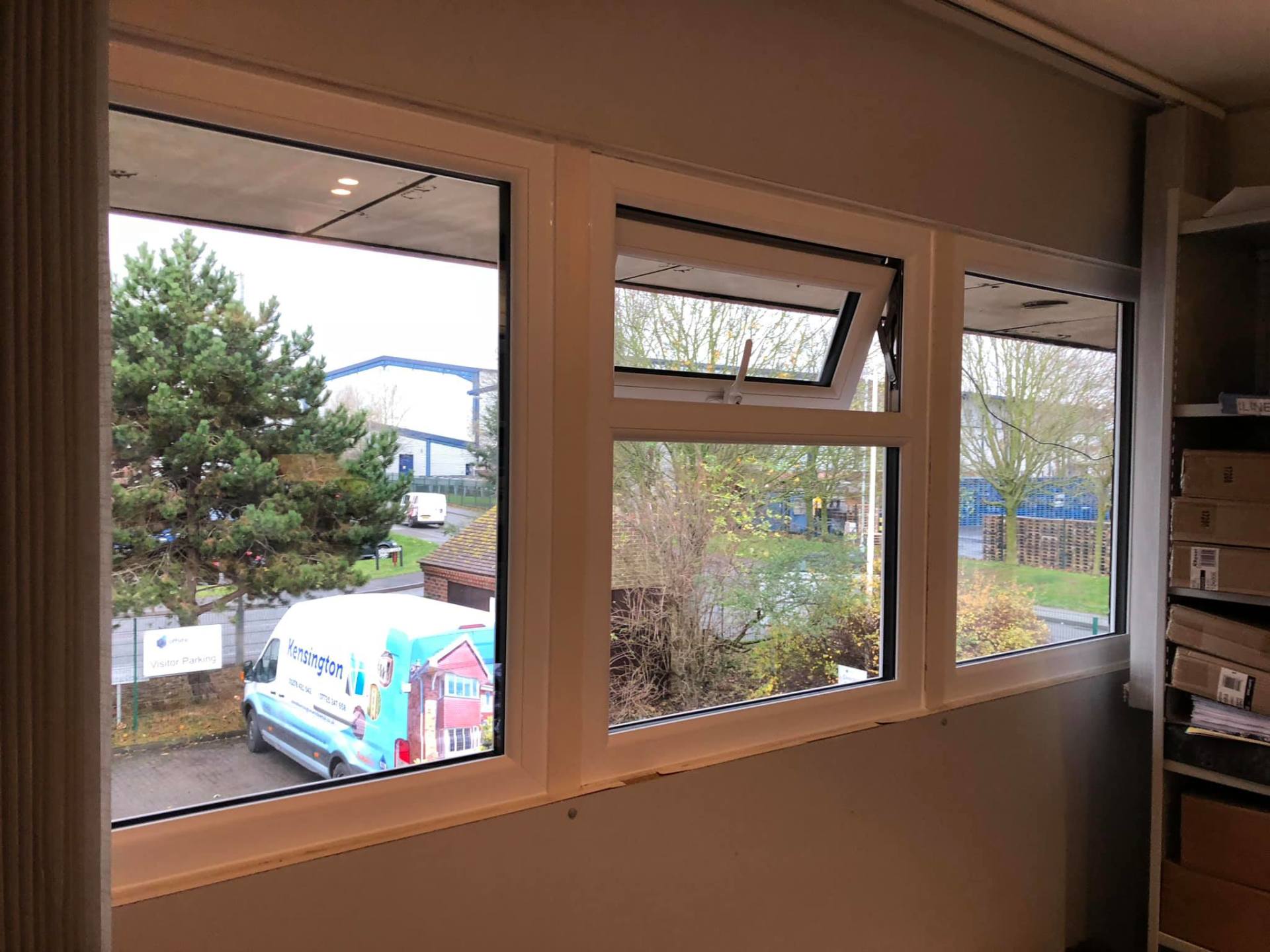 A white van is parked in front of a window in a room.