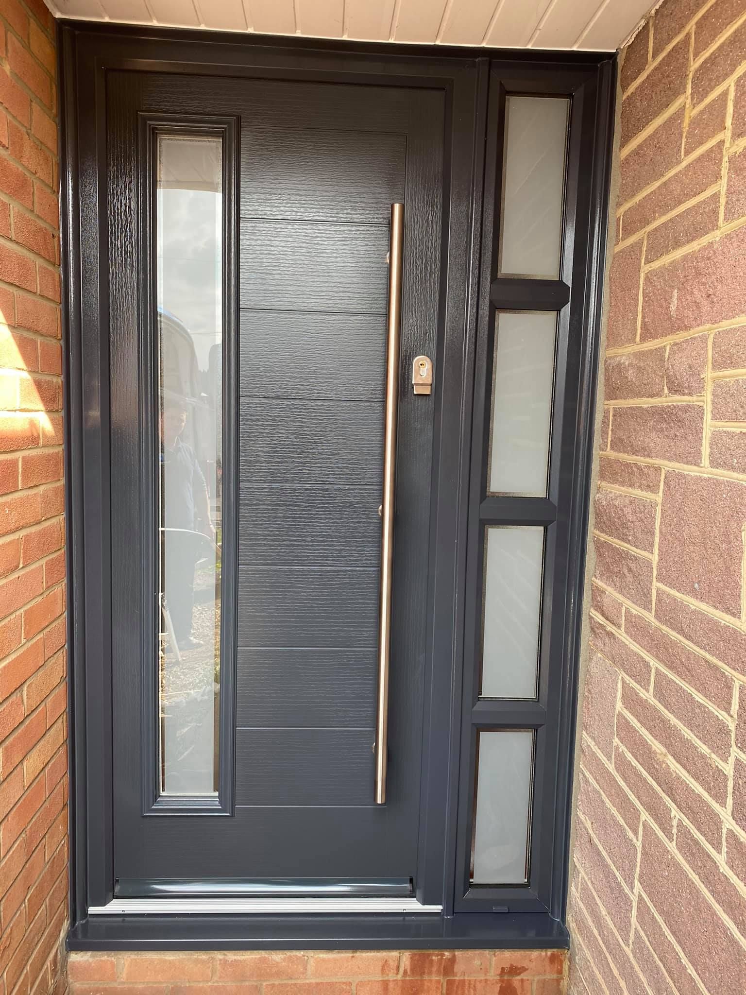 A black front door with a stainless steel handle is on a brick wall.