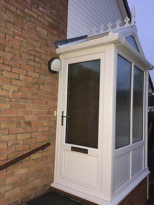 A white porch on the side of a brick house.