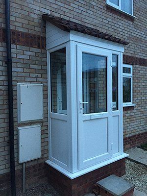 A white porch on the side of a brick house.