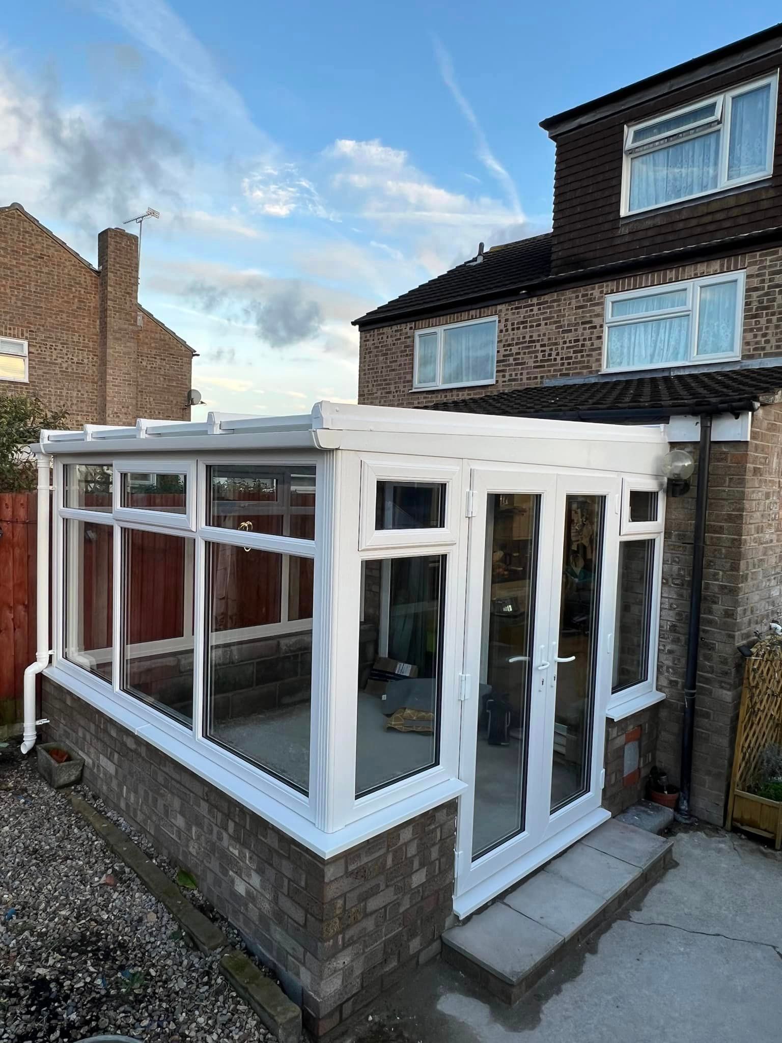 A white conservatory is sitting next to a brick house.