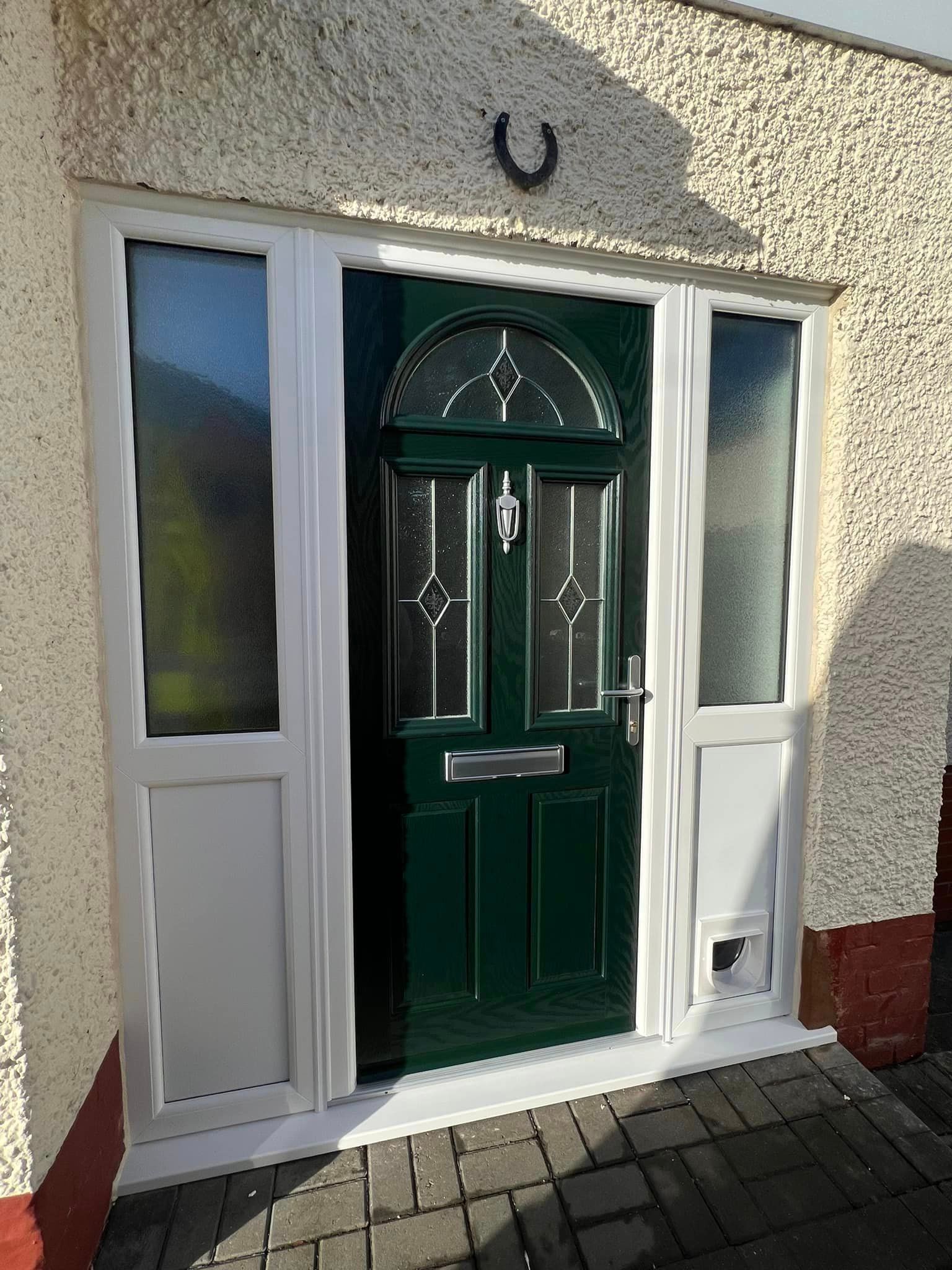A green door with a horseshoe on top of it is on the side of a house.