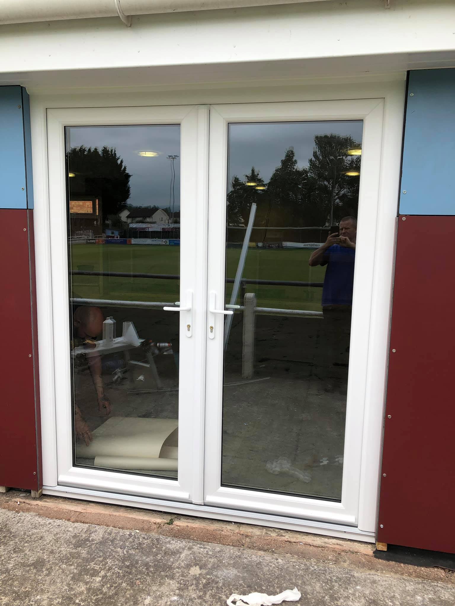 A man is taking a picture of a field through a glass door.