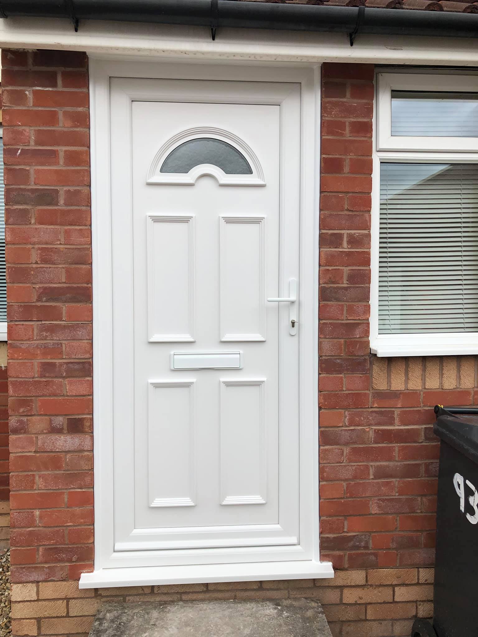 A white door is on a brick wall next to a window.