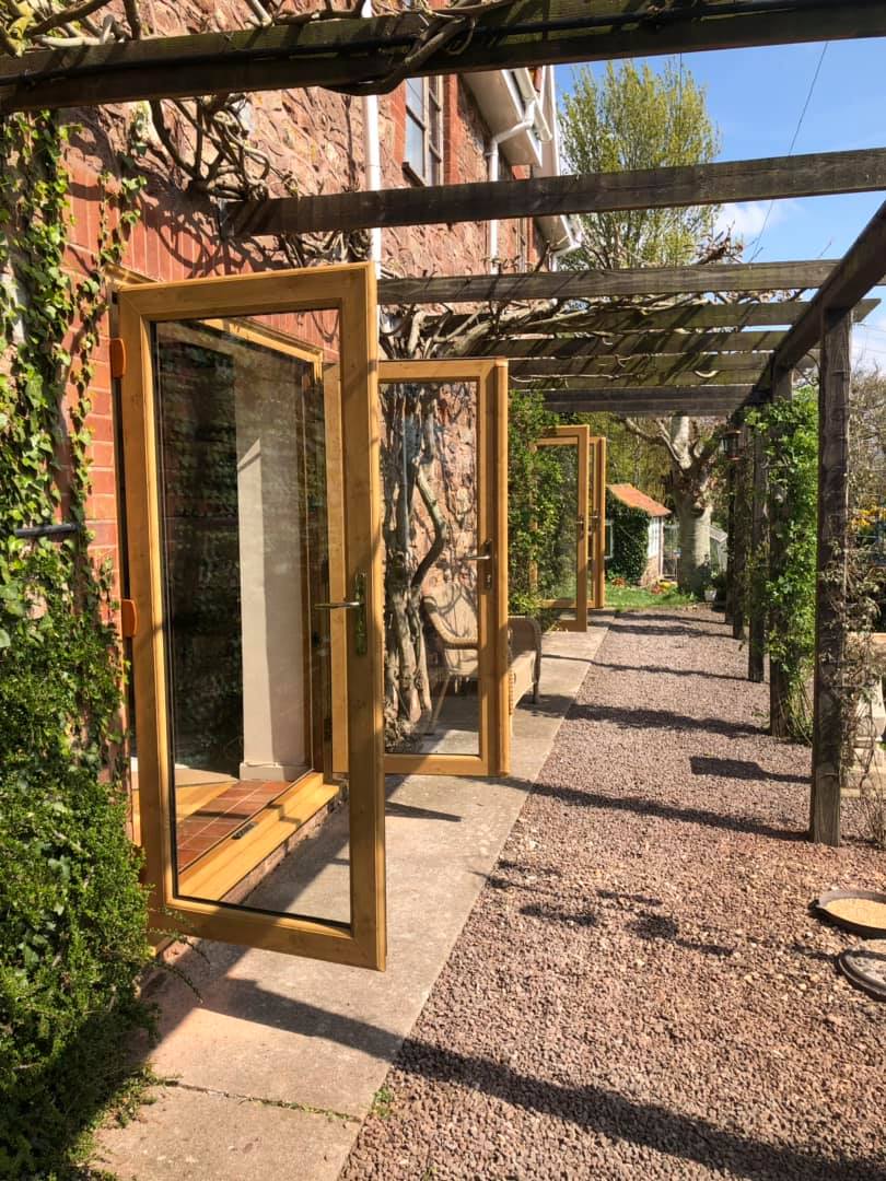 A wooden walkway with a pergola and a brick building in the background.