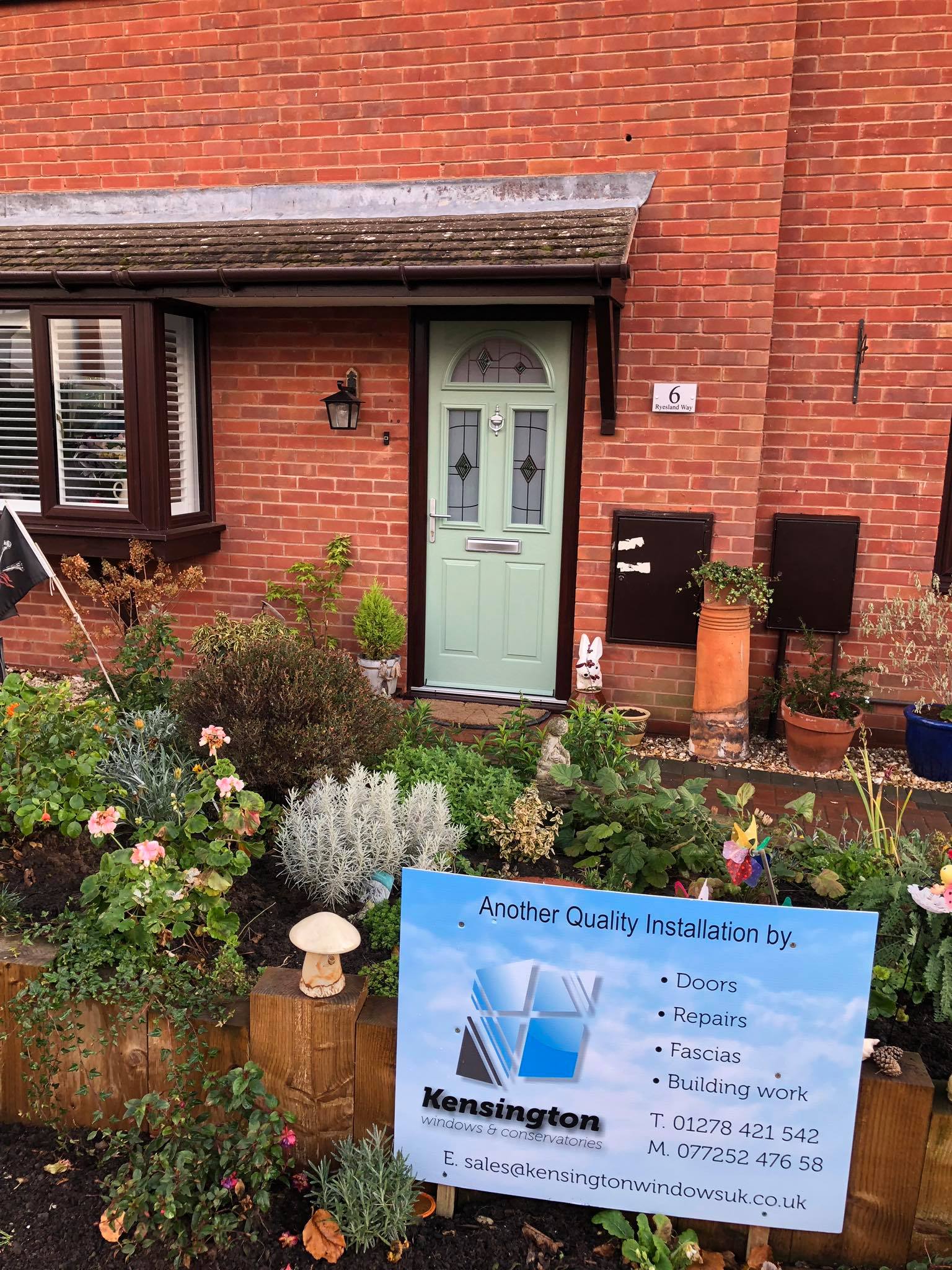 A brick house with a green door and a sign in front of it.