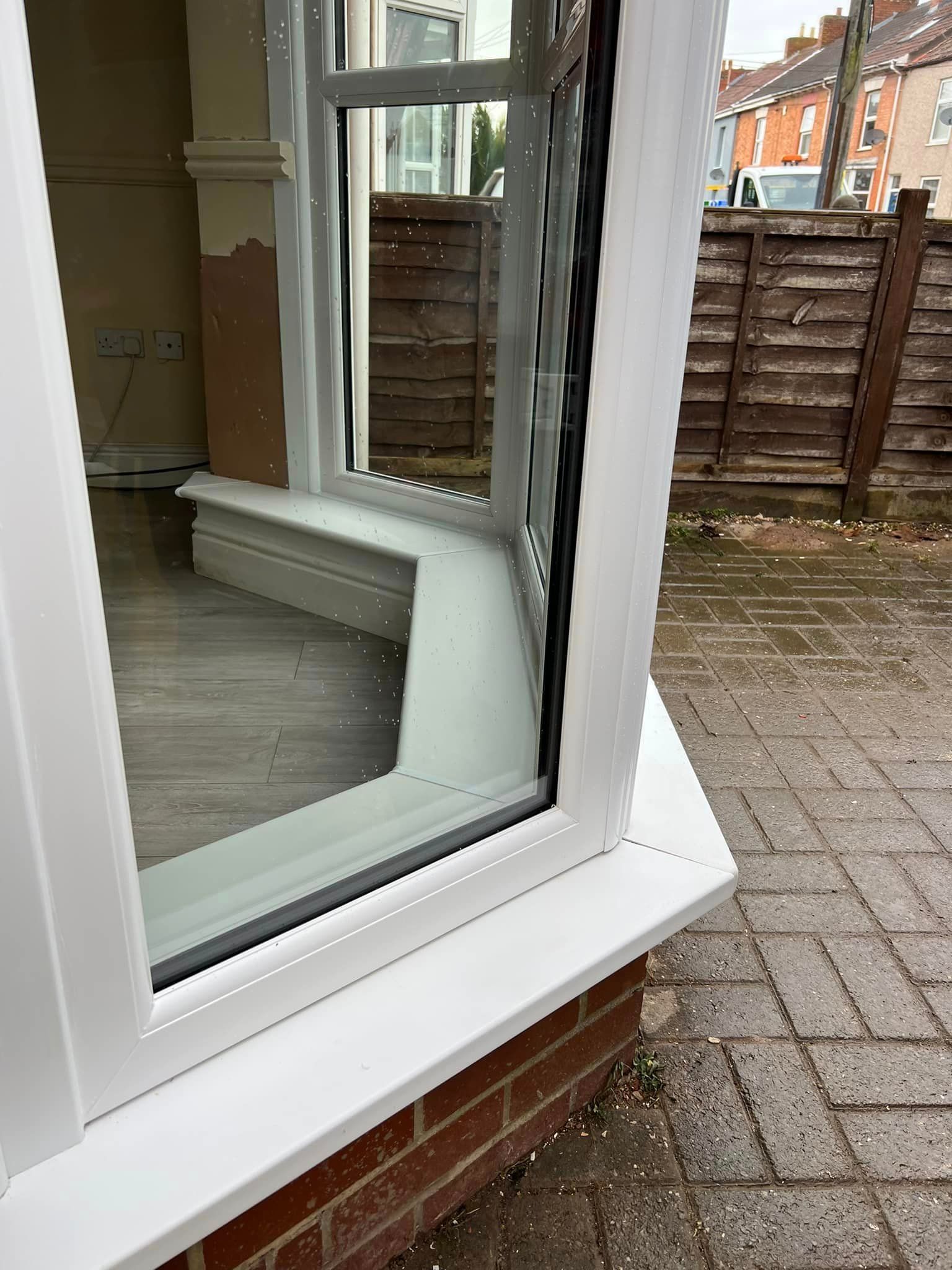A white window is sitting on a brick wall next to a wooden fence.