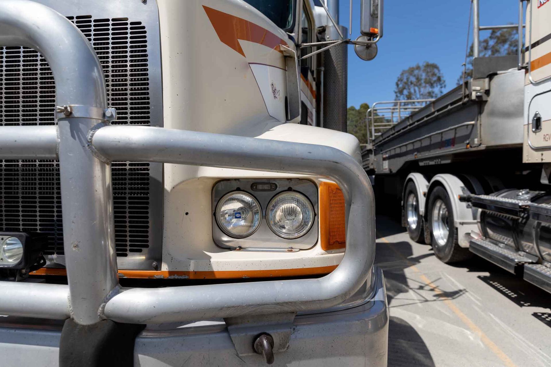 A white semi truck with a chrome bumper is parked on the side of the road.