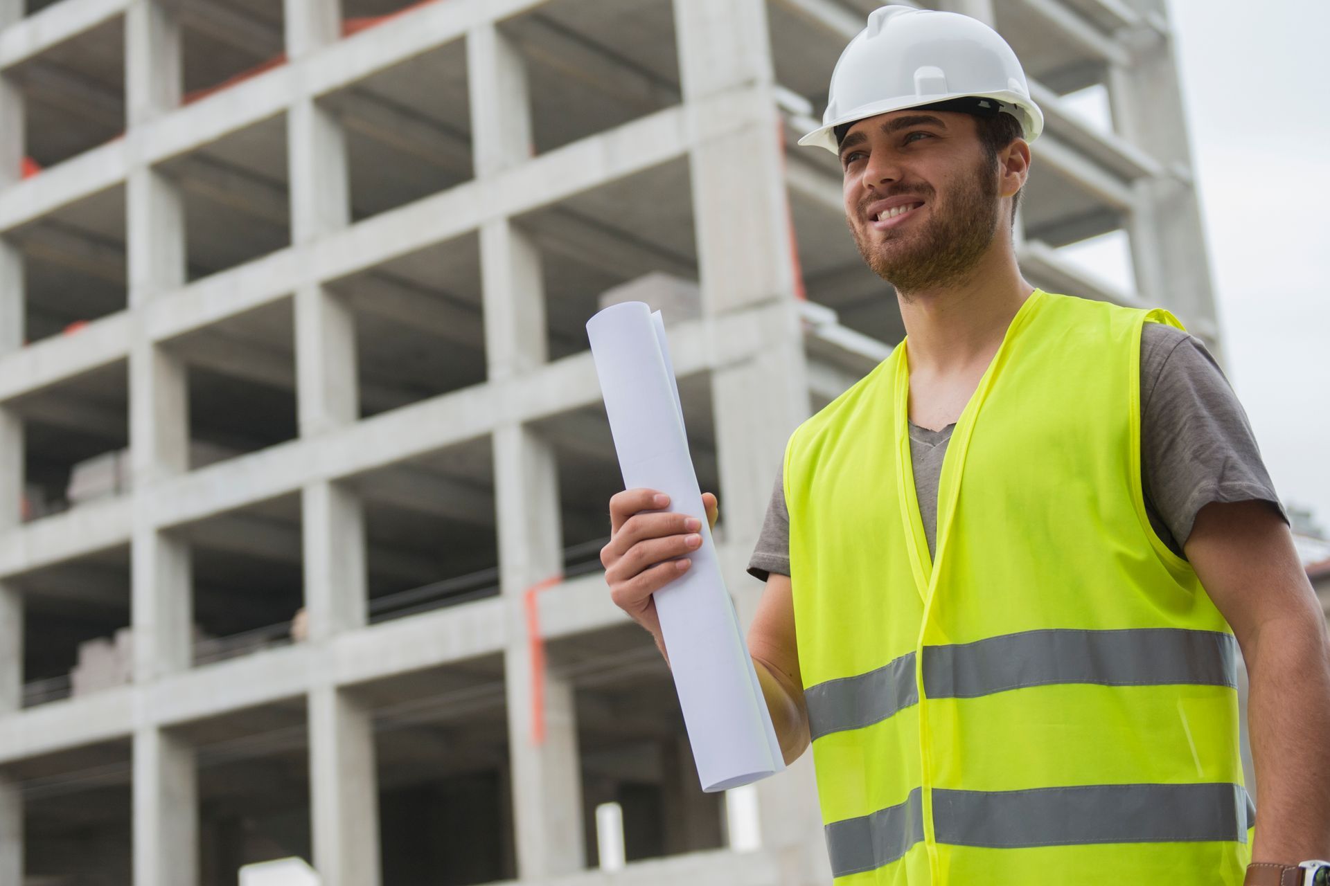 From the control of a building project a civil contractor smiles while holding a blueprint.
