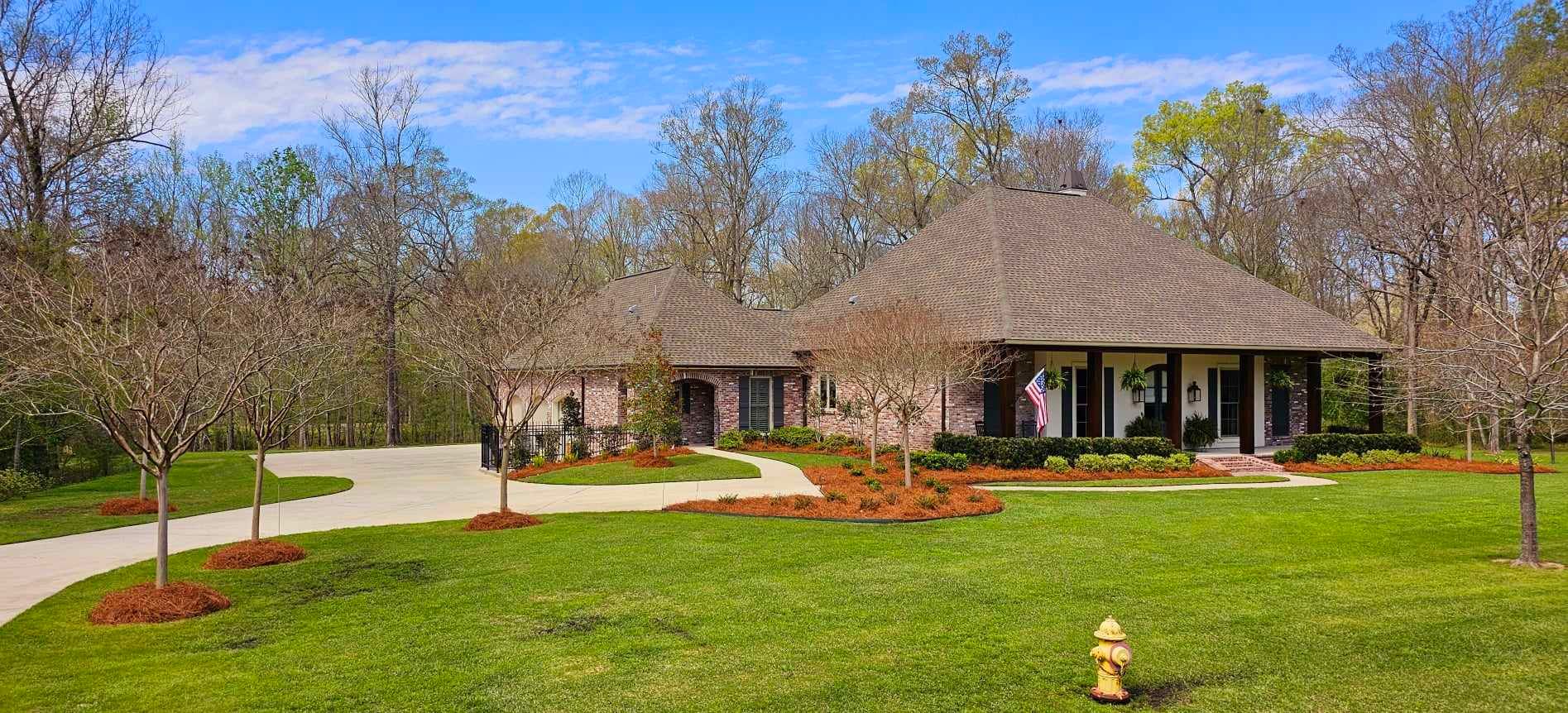 A large house with a fire hydrant in front of it is surrounded by trees and grass.