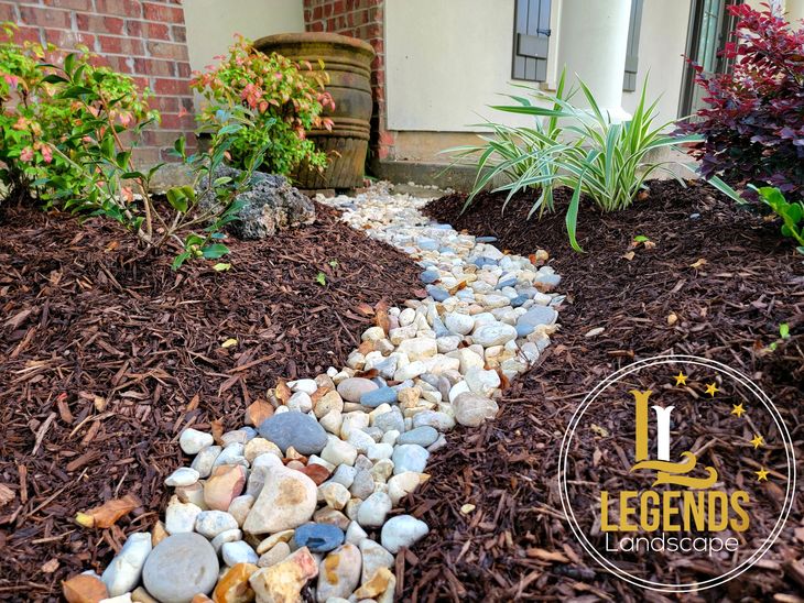 A walkway made of rocks and mulch in front of a house.