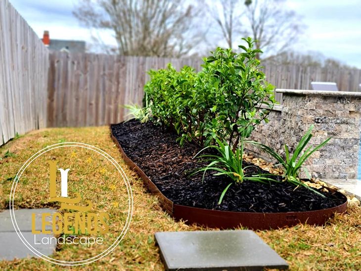 A garden with a fence in the background and a sign that says legends landscape