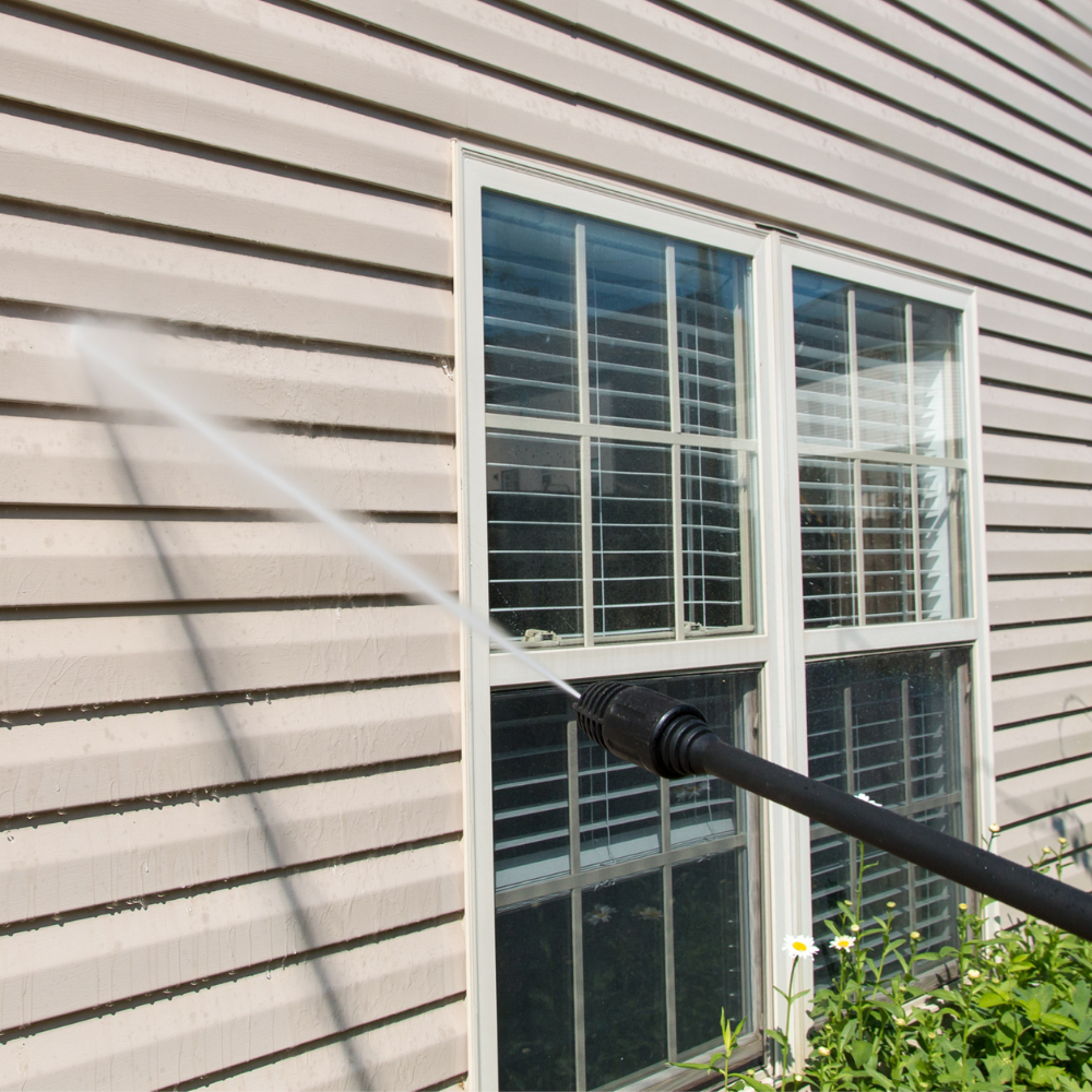 A person is cleaning the side of a house with a high pressure washer.