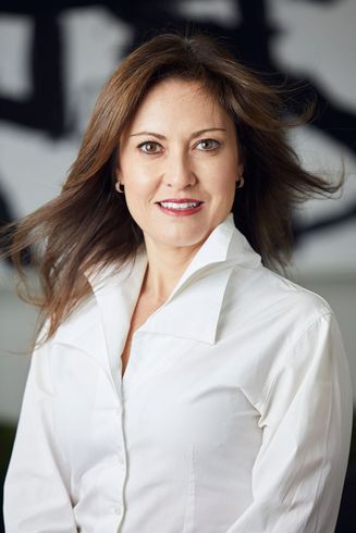 Woman in a white shirt smiles, hair blowing, against a blurred art backdrop.