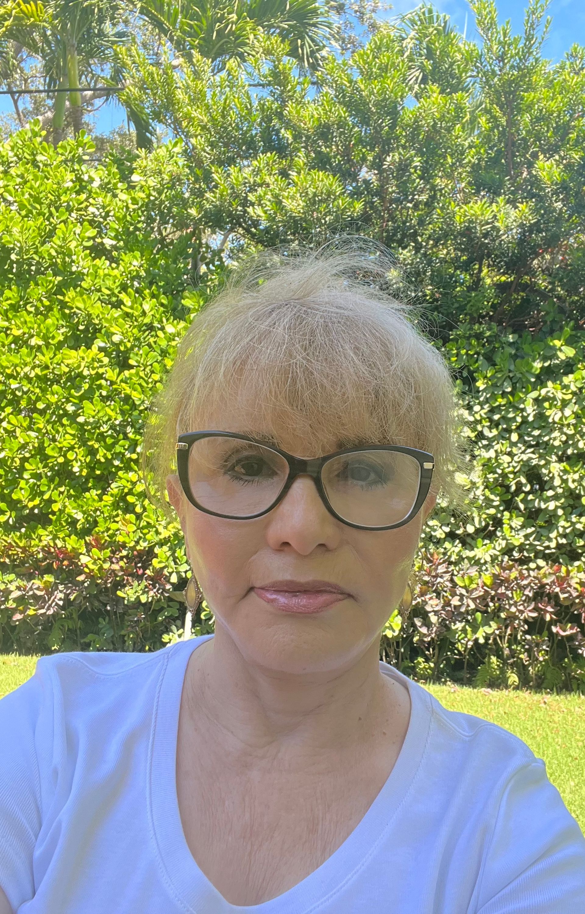 Woman with blonde hair and glasses in front of a green, leafy background.