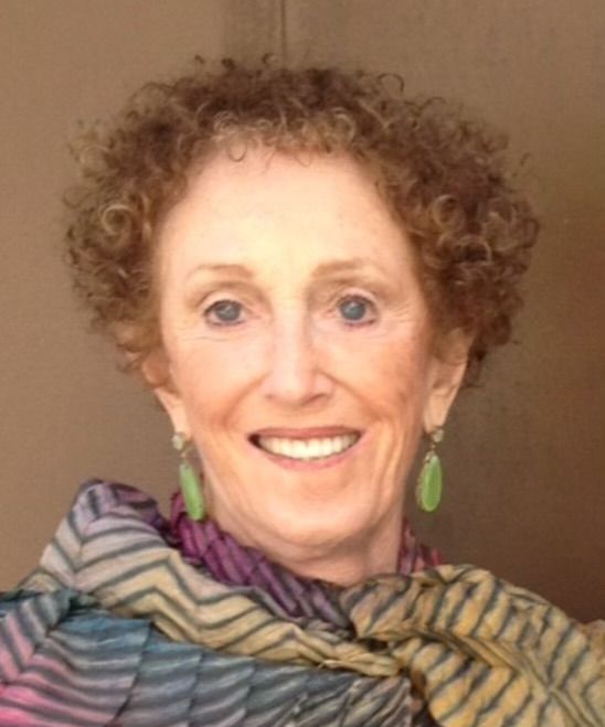 Woman with curly red-brown hair, wearing green earrings and a colorful scarf, smiling.