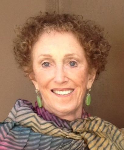 Woman with curly red-brown hair, wearing green earrings and a colorful scarf, smiling.