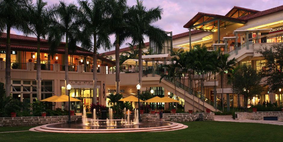 Palm trees frame a lit-up outdoor shopping center with fountains and seating.