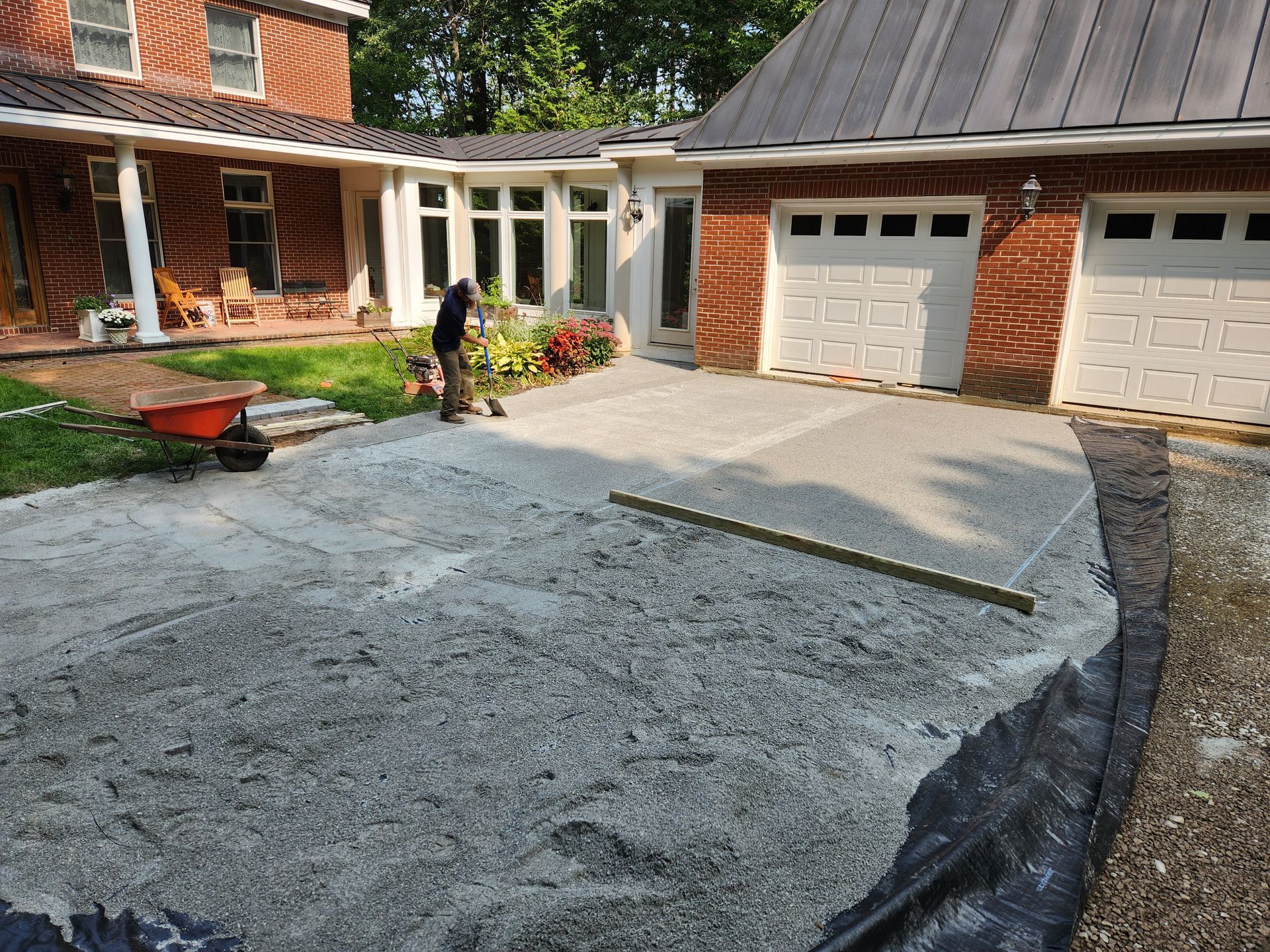 Man leveling wet concrete for a driveway, next to a house and garage with white doors.