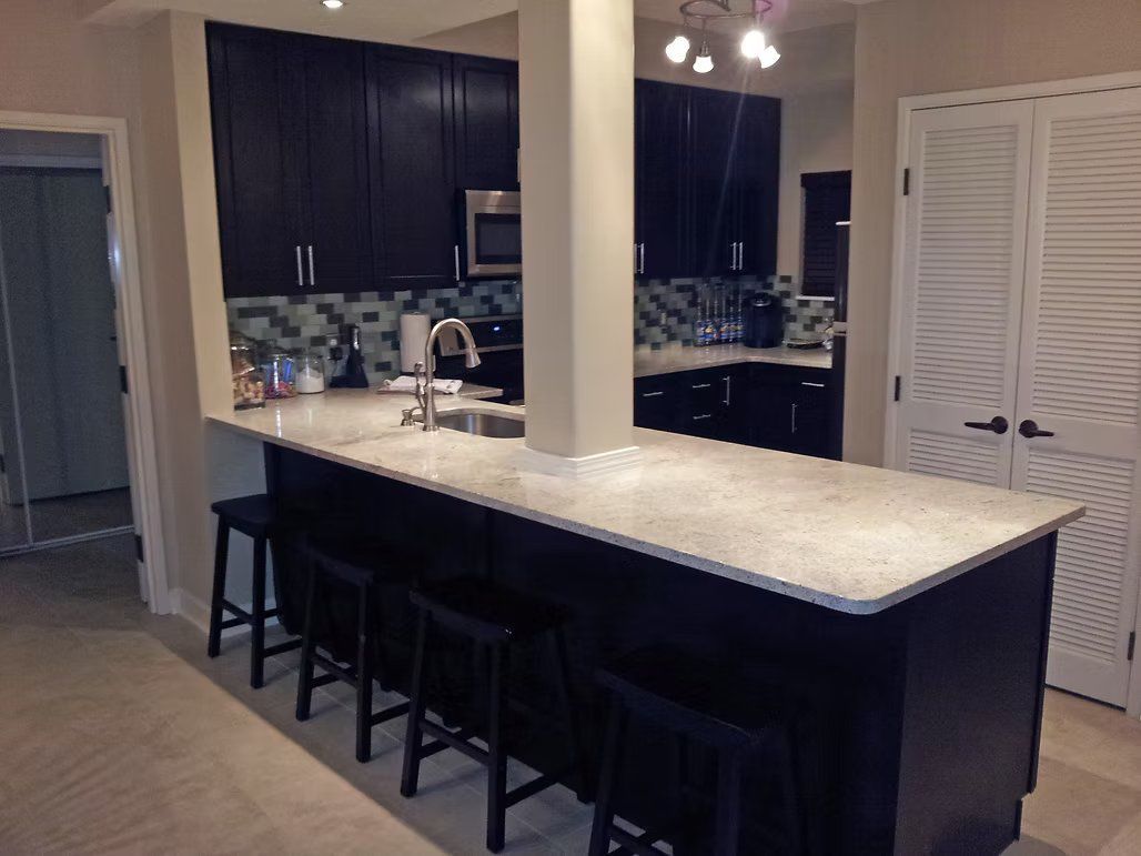 Kitchen with black cabinets, white countertop, island with stools, and white doors.