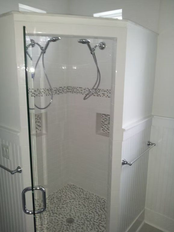 White tiled walk-in shower with dual shower heads, glass door, and pebble floor.