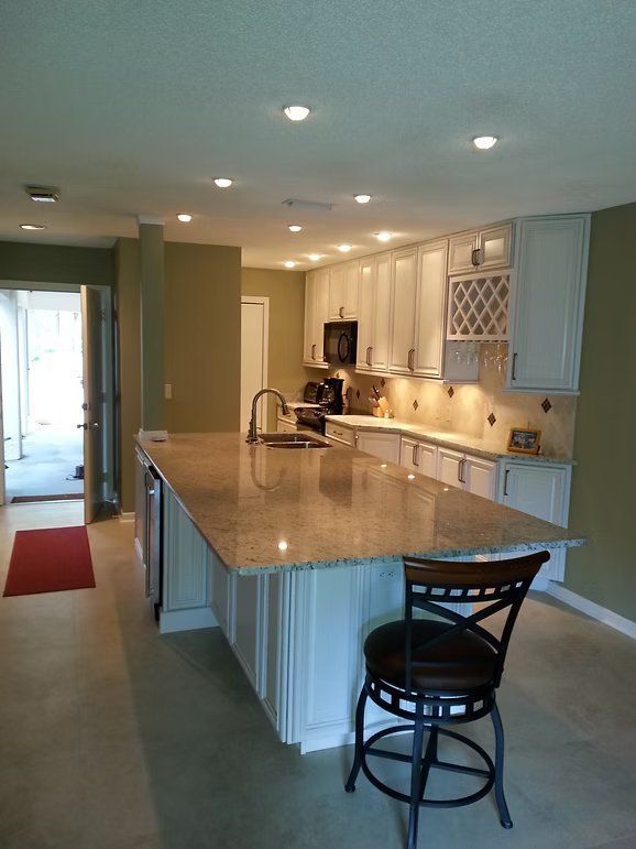 Kitchen with white cabinets, granite countertop island, and a bar stool.