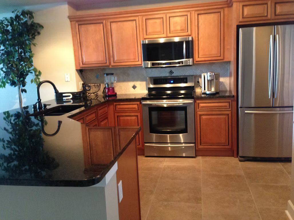 Kitchen with wood cabinets, black countertops, stainless steel appliances, and tile floor.