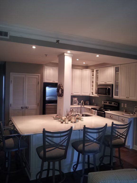 Kitchen with white cabinets, island with stools, and built-in appliances.