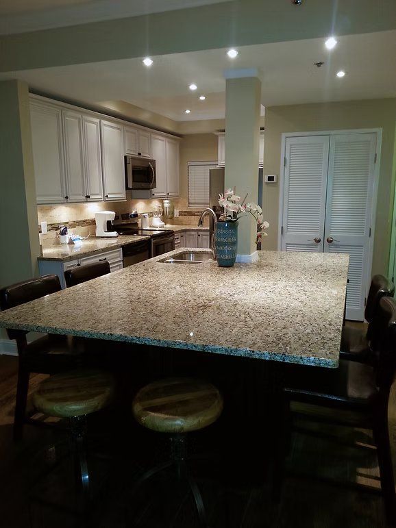 Kitchen with light cabinets, granite countertops, island with stools, and white shutter doors.