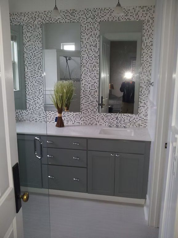 Bathroom with gray vanity, two mirrors with patterned tile, and white walls.