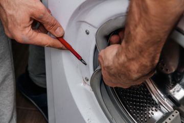 A man is fixing a washing machine with a pencil.