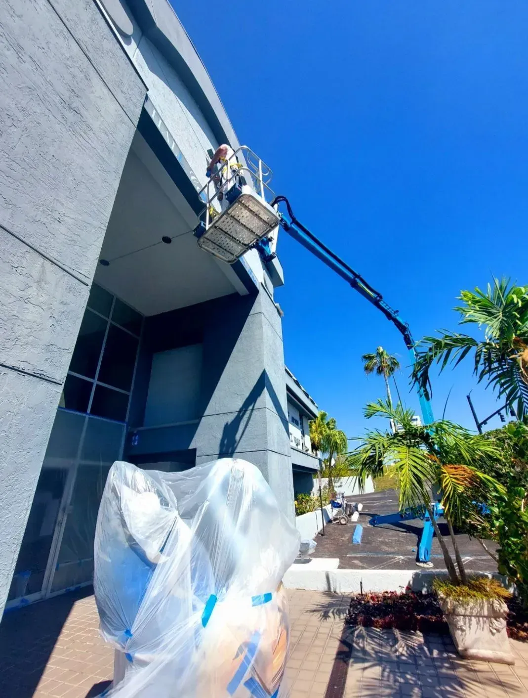A man in a bucket is painting the side of a building