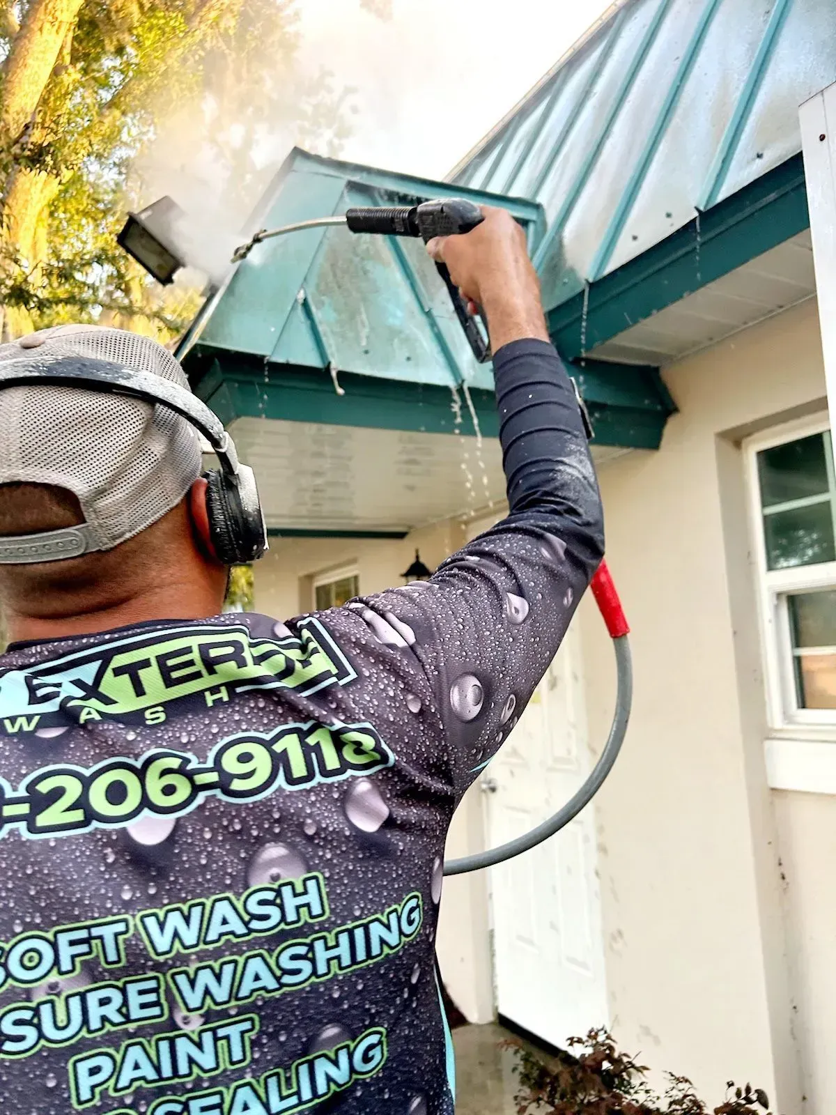 A man is cleaning the roof of a house with a pressure washer.
