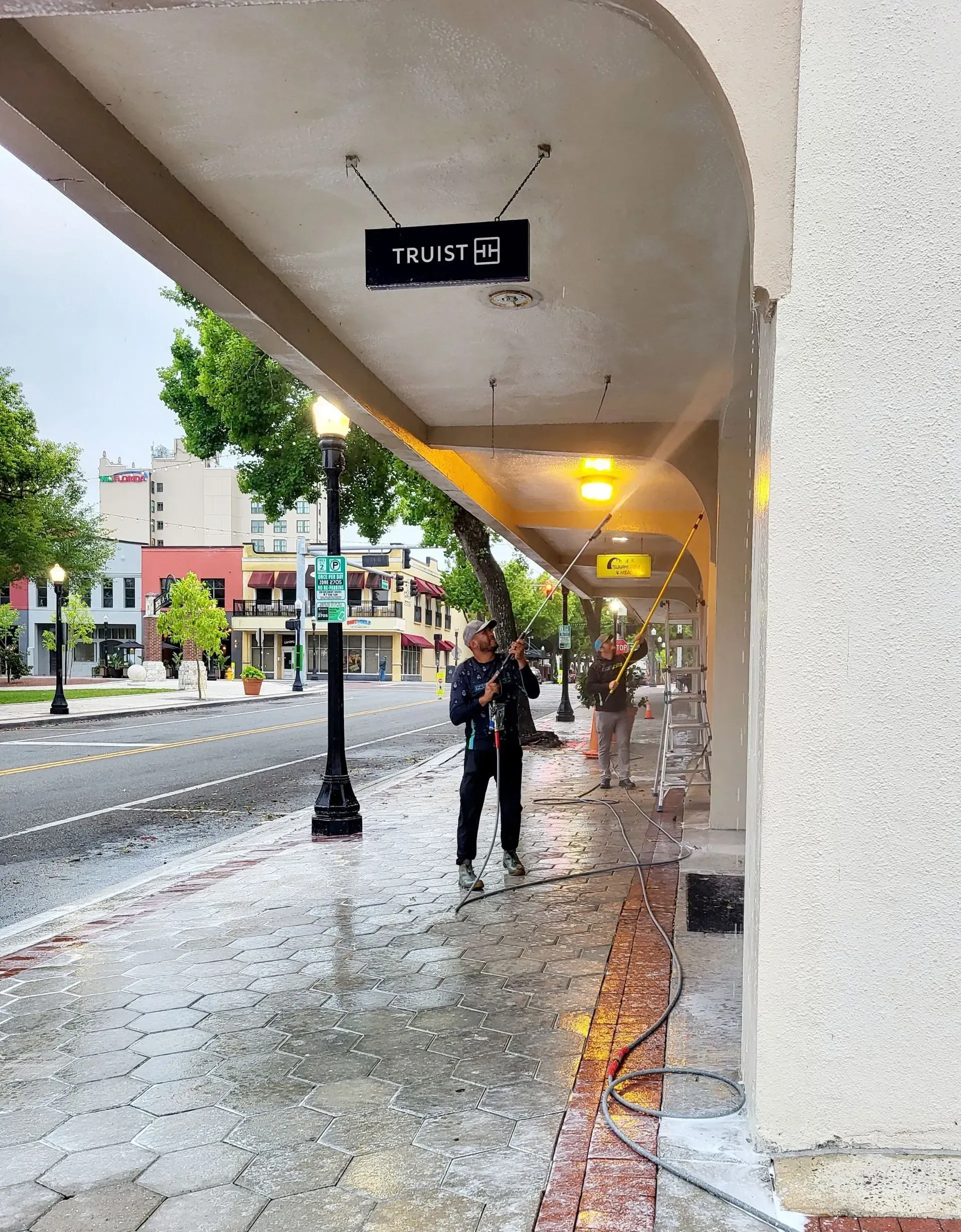 A man is walking down a sidewalk in the rain under a sign that says trust