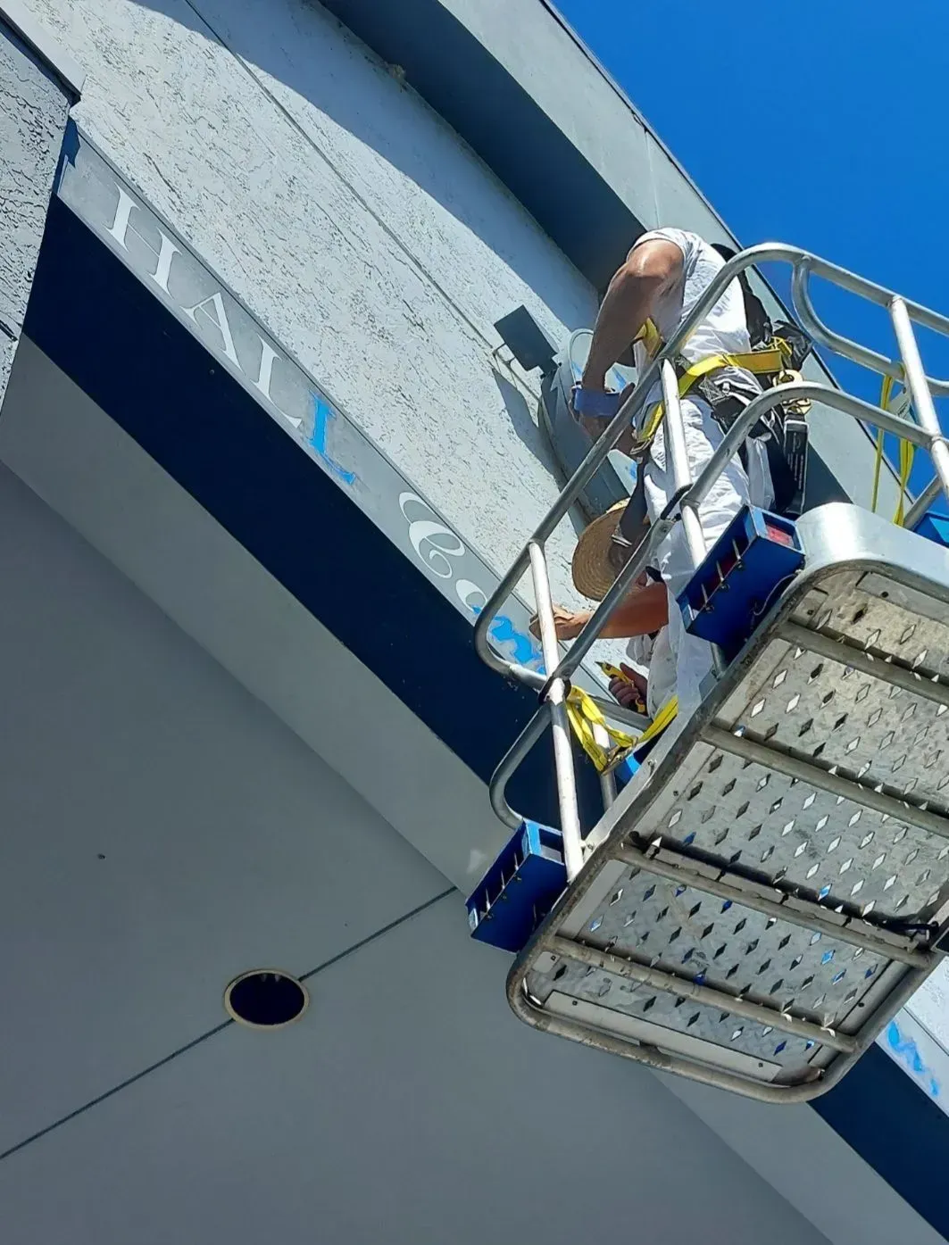 A man in a bucket is painting a sign on the side of a building