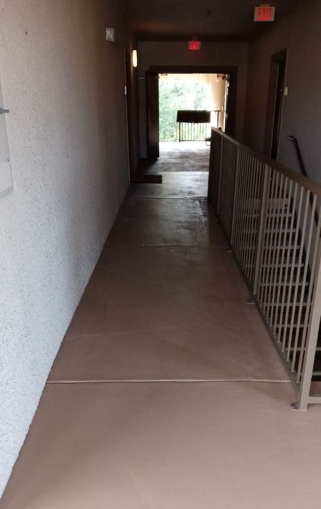 A long hallway with stairs and a red exit sign
