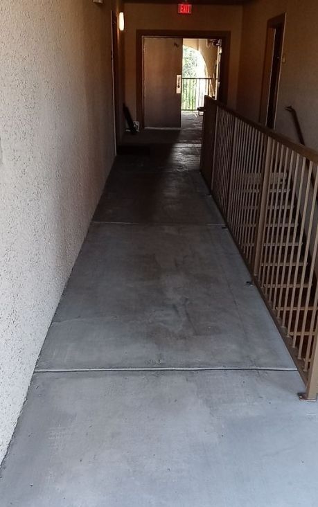 A long hallway with a railing and a red exit sign.
