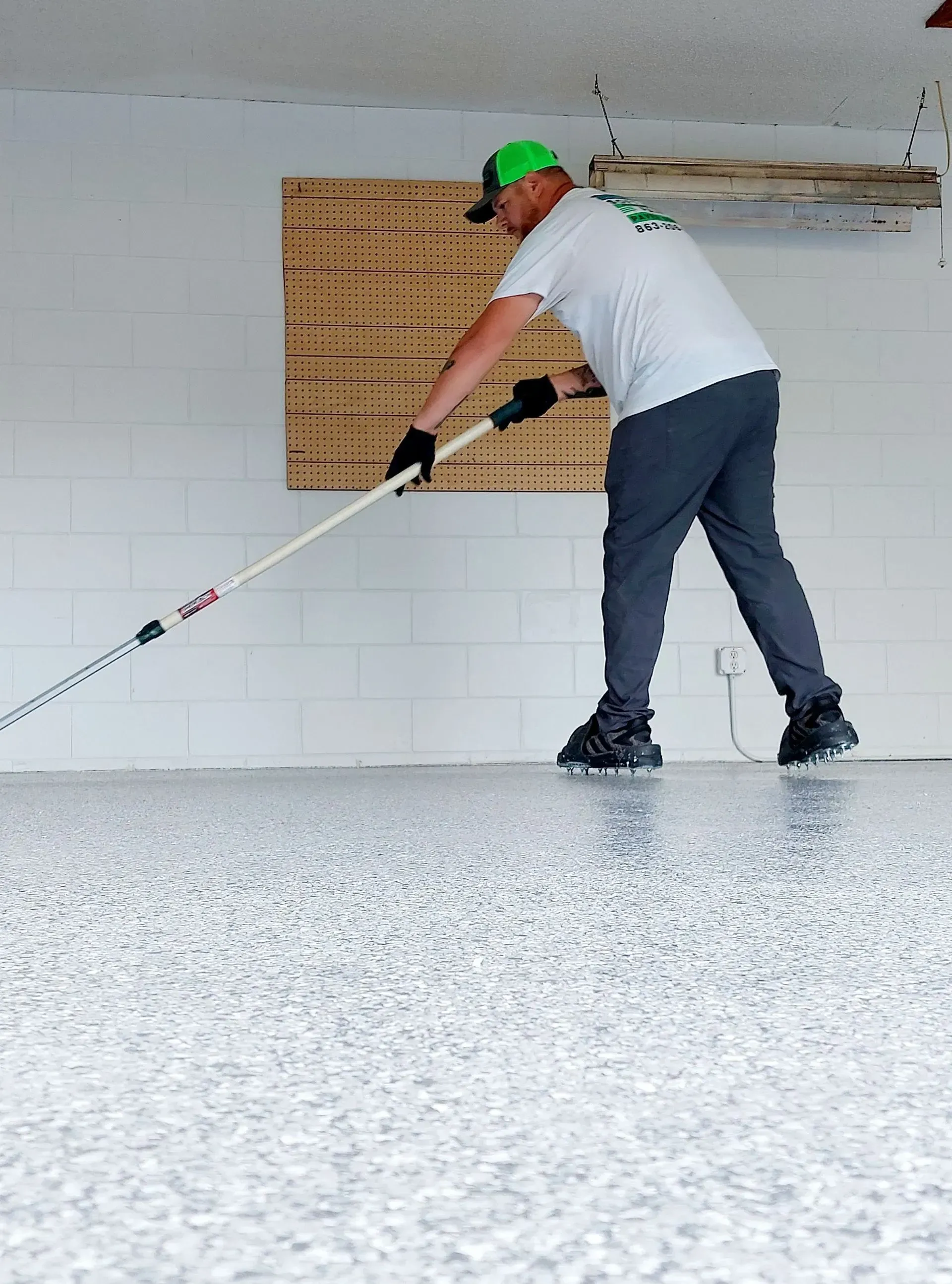 A man is painting a garage floor with a broom.