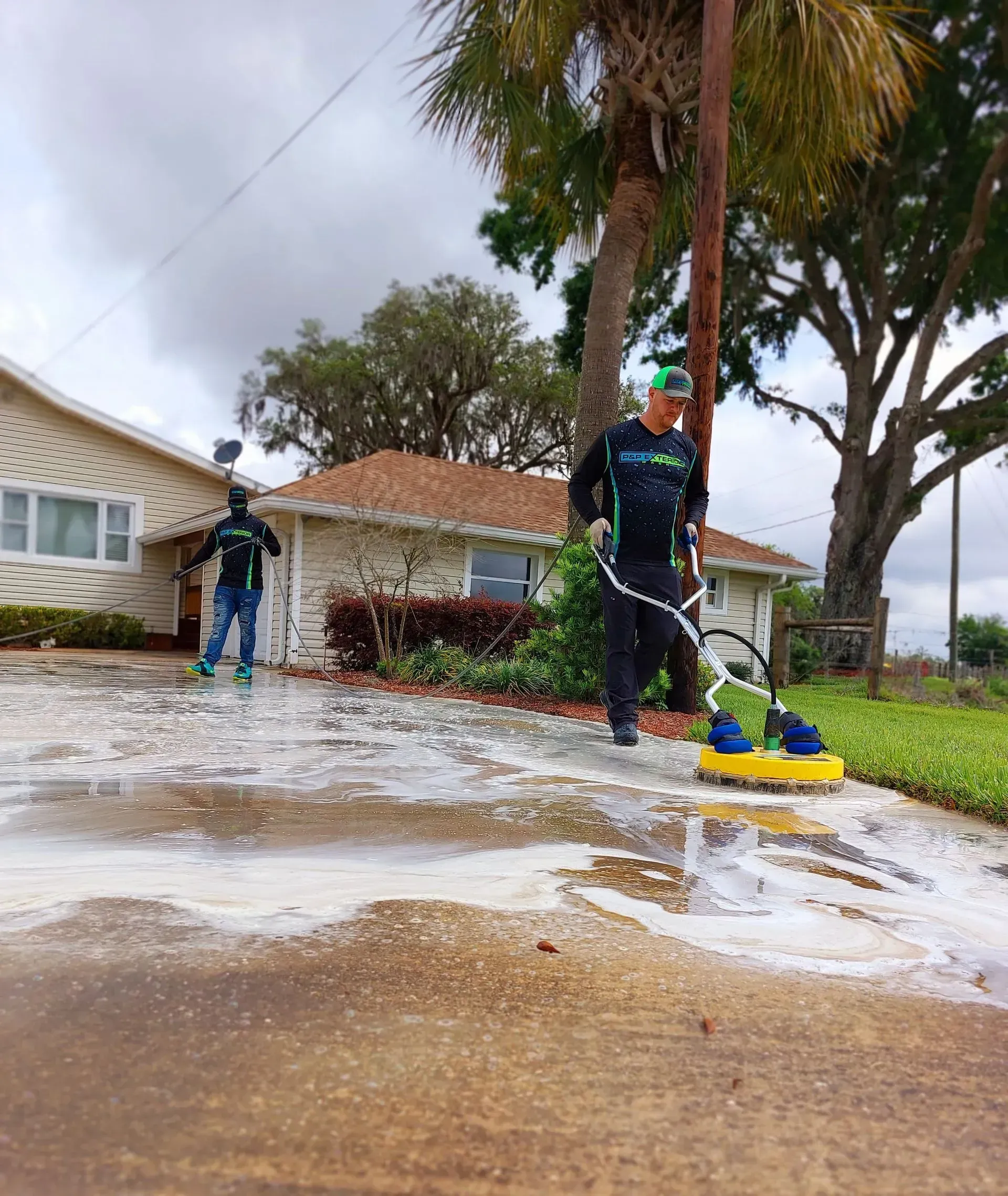 Two men are cleaning a driveway in front of a house.